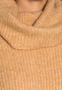 Maglione lavorato a maglia con collo a scaldacuore, realizzato in materiale morbido e strutturato di colore giallo senape chiaro, caratterizzato da un design a coste su tutta la superficie.