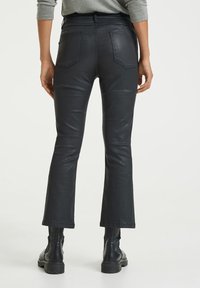Svarta läderbyxor i flaremodell med bakfickor, har en mjuk textur och en midjehöjd som är något nedsänkt, kombinerat med svarta kraftiga stövlar.