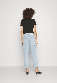 Camiseta negra, pantalones cargo de mezclilla azul claro con múltiples bolsillos, dobladillo recortado y cinturón blanco. Los zapatos son negros, destalonados y con un pequeño tacón.