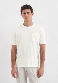 Kurzärmliges, rundhalsiges T-Shirt aus elfenbeinfarbenem Stoff, mit kleiner Brusttasche und relaxed Fit sowie glatter Textur.