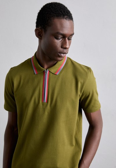 Polo de color verde oliva con mangas cortas, que presenta un cuello con cremallera y detalles en rayas rojas y grises en el cuello. Textura suave.