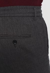 Pantaloni grigi su misura realizzati in un tessuto texturizzato, con chiusura a bottone, tasca a filetto e vita liscia.
