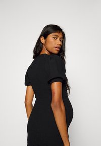 Vestido preto de mangas bufantes com textura plissada, silhueta ajustada e decote redondo. Tecido suave com ligeira elasticidade, usado por uma modelo.