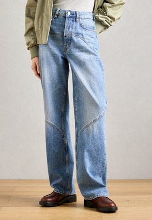 Lyseblå høyhalsede jeans med en avslappet passform, med unike sømdetaljer og synlig søm. Kombinert med brune hælboots.