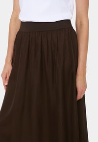 Gonna marrone fino al ginocchio con una larga fascia elastica in vita e una texture arricciata. Tessuto liscio che offre un design fluido.