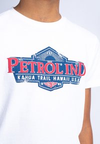 Weißes Baumwoll-T-Shirt mit grafischem Design und rot-blauer Beschriftung. Der Druck enthält "PETROL IND" und "KAHUA TRAIL HAWAII, U.S.A."