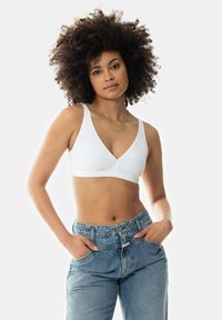 Witte geribbelde beha met een V-halsontwerp en brede banden, gecombineerd met high-waisted blauwe denim jeans met een relaxte pasvorm en flinke voorzakken.