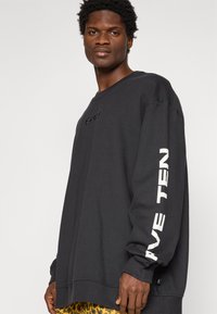 Juodas džemperis iš minkštos medžiagos su apvaliomis kaklo apačiomis, ant kairiojo rankovės esančiu "FIVE TEN" ryškiu balto teksto užrašu. Laisvas kirpimas su ilgomis rankovėmis.