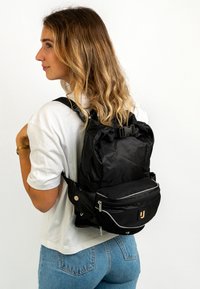 Fekete, nylon hátizsák állítható pántokkal, elülső cipzáras zsebbel és logós hangsúlyozással. Texturált felülettel és elegáns dizájnnal rendelkezik.