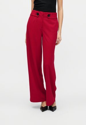 Woman wearing high-waist red wide-leg trousers with black buttons, paired with black pointed-toe shoes and a black sleeveless top.