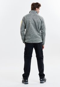 Grå, texturerad fleecejacka med hög krage, i kombination med svarta cargobyxor. Funktioner inkluderar fickor med dragkedja och slitstarka skor.