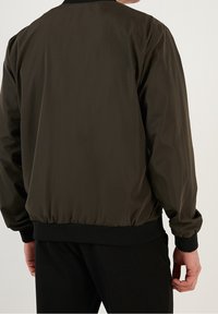 Oliivivihreä bomber-takki, jossa on sileä pinta, ribattu hihansuu ja vyötärö, esitetty klassisessa designissa, nähtynä takaa.