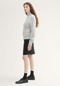 Hellgrauer gerippter Pullover, knielange schwarze Rock, schwarze Schnürschuhe und schwarze Socken. Gerade Silhouette, lässiges Design und strukturierter Stoff.