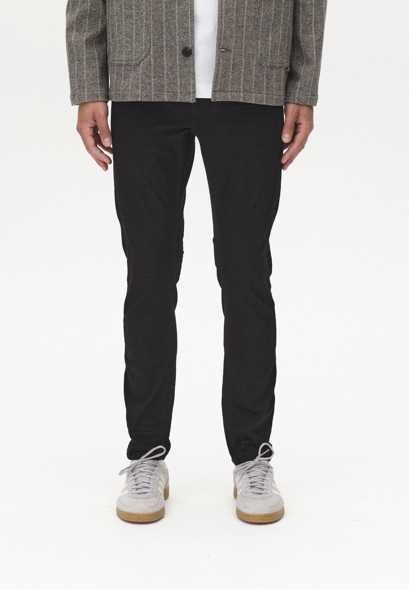 Veste rayée grise sur une chemise blanche, assortie à un pantalon slim noir et des baskets gris clair avec une semelle beige.