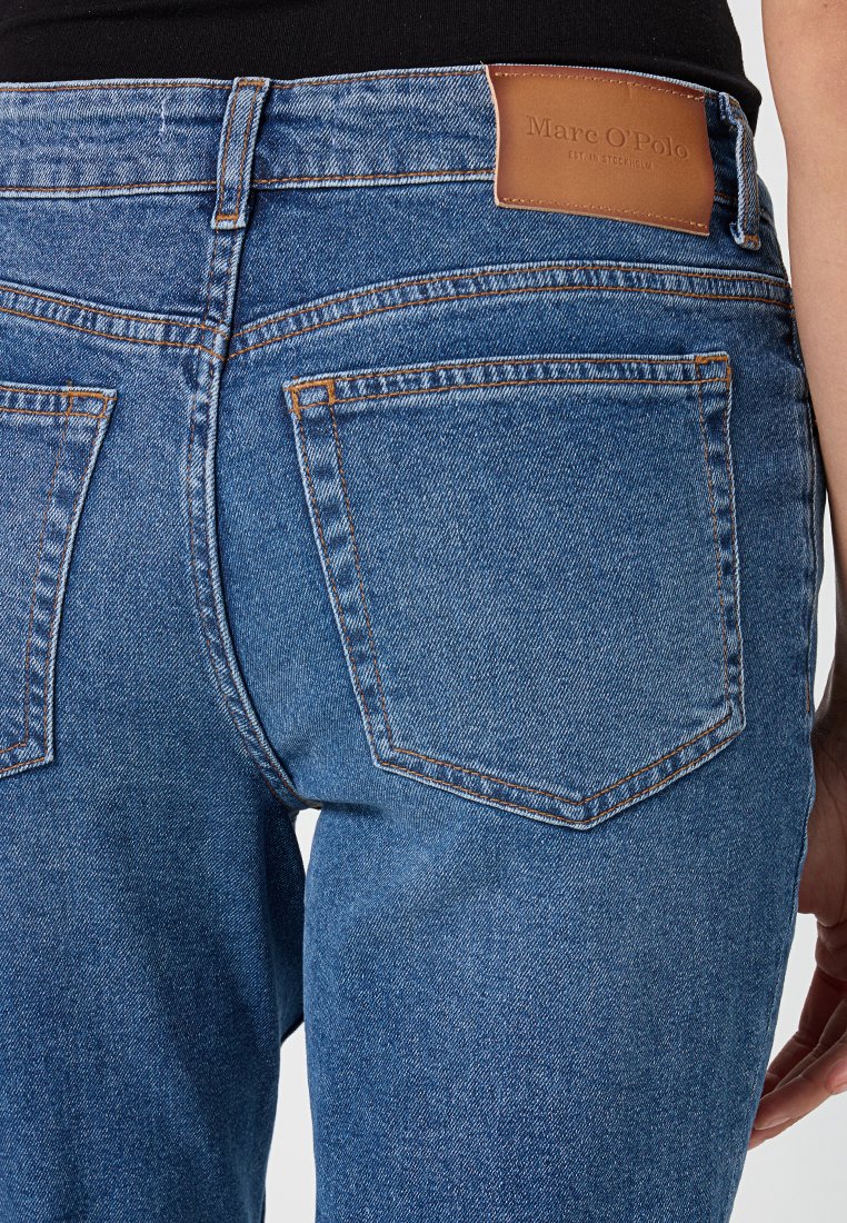 Achteraanzicht van blauwe denim jeans met oranje stiksel en een bruine leren merklabel van Marc O'Polo op de tailleband.