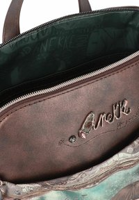 Braune Kunstleder-Handtasche mit silberfarbener Reißverschluss, ausgestattet mit einer strukturierten Oberfläche, einem geprägten Etikett und einem gemusterten Innenfutter.