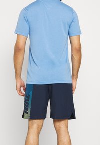 Camiseta de manga corta azul claro combinada con pantalones cortos azul marino que presentan un patrón degradado en verde y amarillo en el costado y dobladillos divididos para facilitar el movimiento.