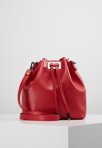 Rød læder spandtaske med snorelukning, justerbar rem og metalliske hardware-detaljer. Glat tekstur og rund form.