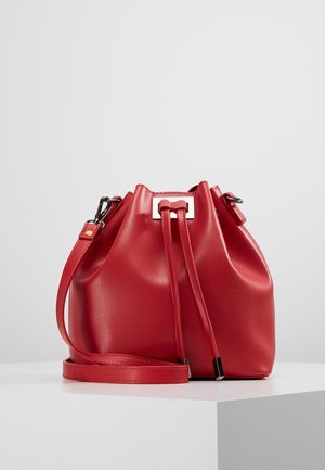 Punainen nahkainen ämpärilaukku, jossa on nyöri sulkemiseksi, säädettävä olkahihna ja metalliset yksityiskohdat. Silkkinen pinta ja pyöreä muoto.