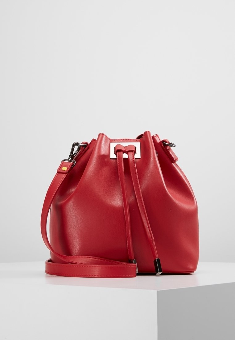 Rød læder spandtaske med snorelukning, justerbar rem og metalliske hardware-detaljer. Glat tekstur og rund form.
