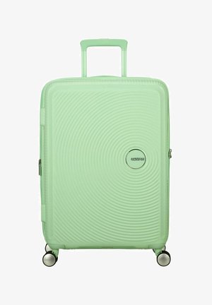 Hard-shell suitcase in mint green, featuring a wave pattern, retractable handle, and four wheels for mobility. Zipper closure and brand logo.