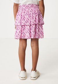 Gonna a strati rosa con motivi geometrici in viola e rosa. Vita elastica. Indossata con sneakers bianche con accenti dorati.
