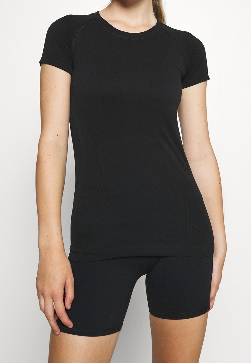 T-shirt de sport noir en tissu extensible, avec des manches courtes, un col rond et une coupe ajustée, associé à un short noir assorti.