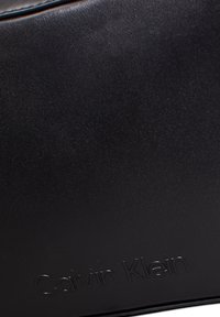 Black leather handbag featuring a smooth texture, minimalist design, and embossed brand logo. Structured shape with clean lines.