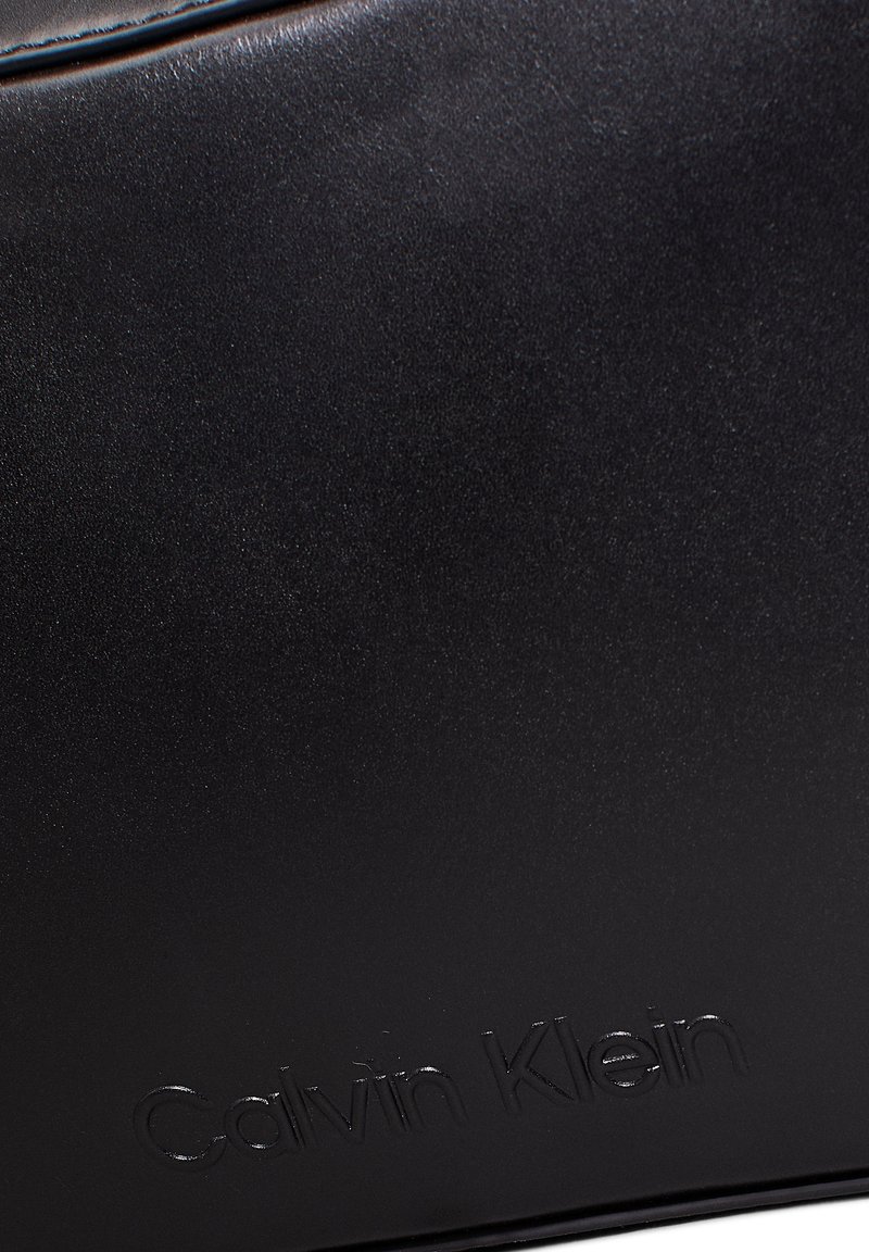 Borsa a tracolla in pelle nera con una superficie liscia, design minimalista e logo del brand impresso. Forma strutturata con linee pulite.