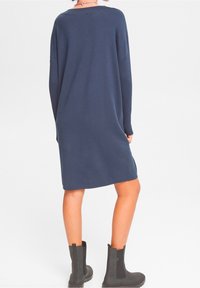 Robe pull en tricot bleu marine avec des manches longues, une coupe décontractée et un col rond, associée à des bottines noires.