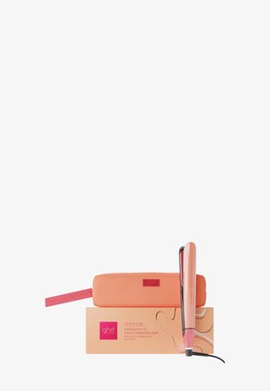 Ferskenfarvet ghd glattejern, der hviler på sin matchende æske ved siden af en lynlåspose med mærket "Good Hair Day".