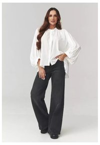 Biała, oversize bluzka z bufiastymi rękawami, zapinana z przodu, w połączeniu z czarnymi, wysokogatunkowymi dżinsami o szerokich nogawkach i czarnymi butami na platformie.