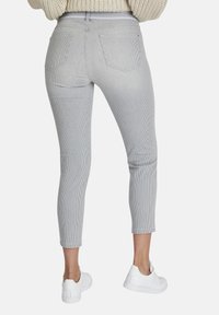 Pantalones ajustados a rayas grises y blancas con cintura alta, que cuentan con bolsillos traseros, combinados con zapatillas blancas sobre un fondo neutro.