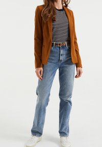 Brun skräddarsydd blazer över en marinblå och vit randig topp, kombinerad med ljustvättade raka jeans och vita sneakers.