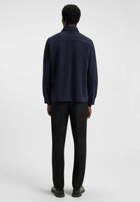 Camicia a maniche lunghe blu navy con colletto, caratterizzata da una vestibilità dritta e polsini con bottone. Indossata con pantaloni neri e scarpe nere.
