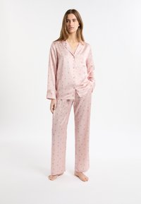 Conjunto de pijama de satén rosa que incluye una blusa con botones, un bolsillo y mangas largas, y pantalones a juego de corte holgado decorados con pequeños estampados florales.