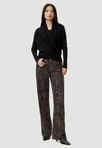 Jersey negro con mangas largas, combinado con pantalones de pierna ancha con un estampado de leopardo marrón. La modelo está de pie frente a un fondo neutral.