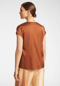 Top marrone a maniche corte con texture liscia, orlo curvo e design sobrio. Abbinato a pantaloni in satin pesca che presentano un effetto gradient.