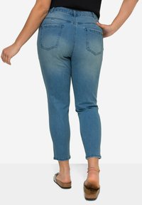 Jeans in denim blu sbiadito con vestibilità slim, vita alta e due tasche posteriori. Il materiale ha una texture liscia. Indossati con sandali marroni.