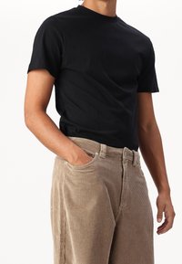 Svart bomulls t-shirt med kort ärm, parat med ljusbruna kordbyxor med ribbad textur och synliga fickor.