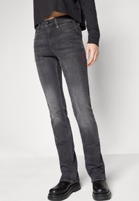Vaqueros negros desgastados de corte slim, diseño de cinco bolsillos, cierre de botón metálico y detalles de costura. Llevados con zapatos de plataforma negros gruesos.