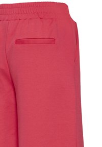 Gros plan sur un pantalon à taille élastique rouge avec poches passepoilées latérales et arrière sur fond blanc uni.