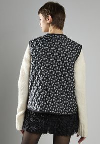 Czarna pikowana kamizelka z białym kwiatowym wzorem, z kontrastowym kremowym swetrem o teksturowanych rękawach oraz warstwową spódnicą w czarne falbany.