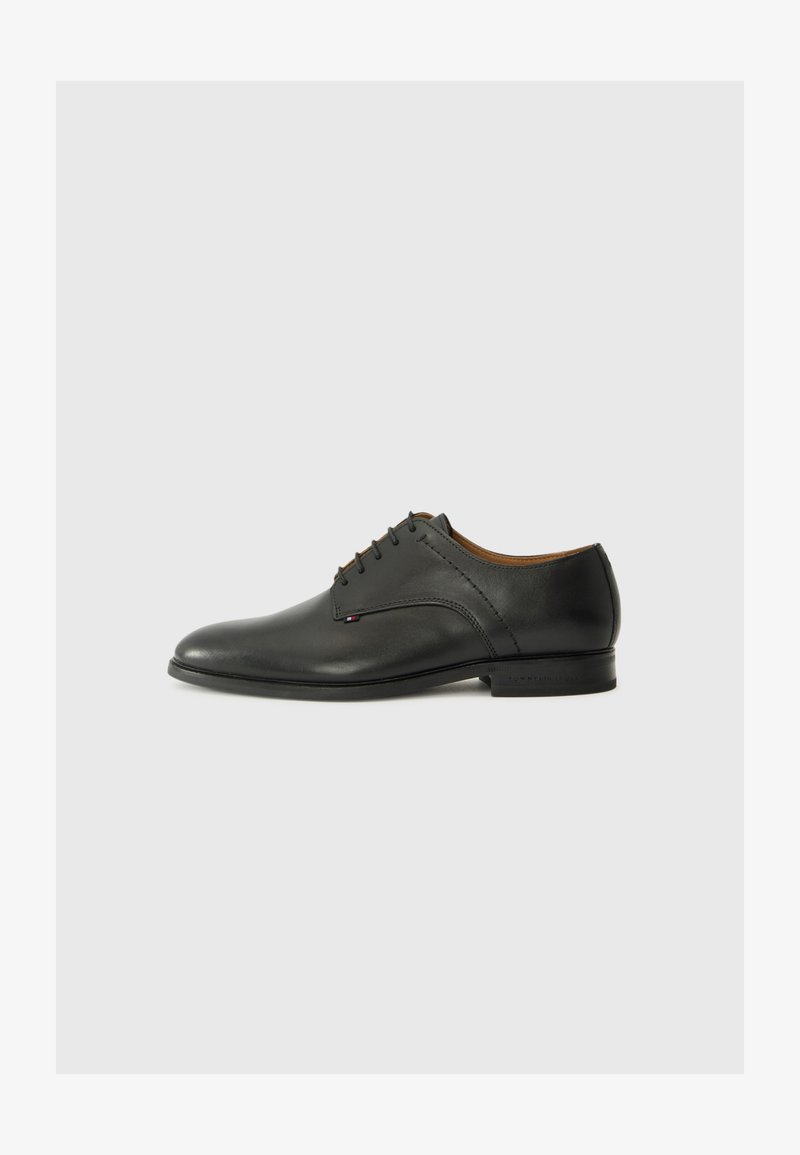 Chaussure de ville en cuir noir avec un bout arrondi, finition lisse, six œillets et un talon bas. Présente une marque discrète sur le côté.