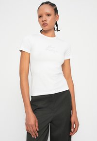 Maglietta bianca aderente con maniche corte, caratterizzata da un sottile ricamo con la scritta "Mixed Feelings" sul petto. Tessuto di cotone liscio.