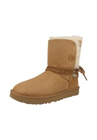 Tan suede ankle boot with a faux fur lining, rounded toe, and patterned laces wrapped around the shaft. Flat rubber sole for traction.
