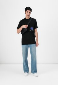Black T-shirt with a graphic print, light blue jeans, and white sneakers. A small black shoulder bag worn across the body.