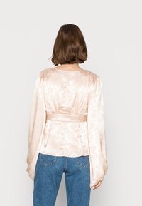 Blusa de satin rosa suave com um padrão floral, mangas largas e uma cintura ajustada. Textura suave e detalhes de design minimalistas.