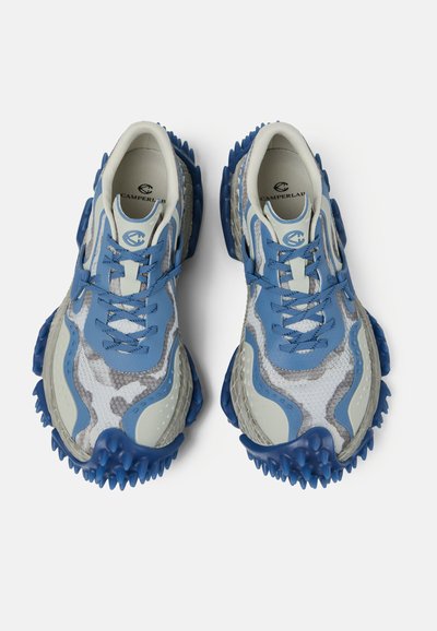 Par de zapatillas texturizadas azul y blanco con suelas con pinchos y cordones, con la marca CamperLab en el interior y en la lengüeta.