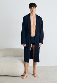 Mornarsko kimono-stil plašč, izdelan iz mehke tkanine, z dolgimi rokavi in odprtim sprednjim delom, nošen nad temnim spodnjim perilom. Enostaven dizajn, brez vzorcev.